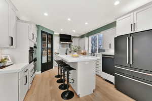 Kitchen featuring dishwasher, light grey cabinets, wall exhaust hood, high end fridge, and a breakfast bar area