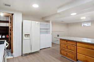 Kitchen with light stone countertops, white fridge with ice dispenser, light hardwood / wood-style floors, and range