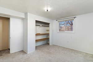 Unfurnished bedroom featuring a textured ceiling, light carpet, and a closet