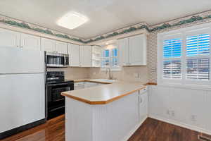 Kitchen featuring black range with electric stovetop, white cabinetry, sink, white refrigerator, and kitchen peninsula