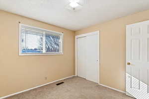 Unfurnished bedroom with a textured ceiling, light carpet, and a closet