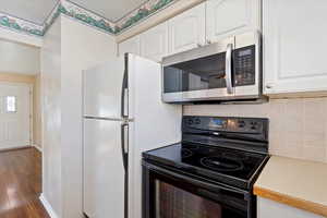 Kitchen featuring tasteful backsplash, electric range, white cabinets, and dark wood-type flooring