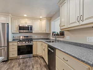 Kitchen featuring cream cabinets, sink, dark hardwood / wood-style floors, a textured ceiling, and appliances with stainless steel finishes