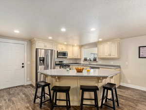 Kitchen featuring a kitchen bar, dark hardwood / wood-style flooring, a textured ceiling, and appliances with stainless steel finishes