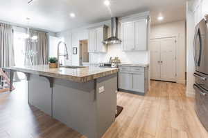 Kitchen with sink, wall chimney exhaust hood, an island with sink, a breakfast bar area, and stainless steel refrigerator