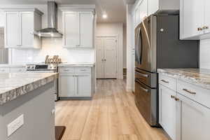 Kitchen with appliances with stainless steel finishes, tasteful backsplash, light stone counters, and wall chimney exhaust hood