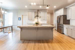 Kitchen with a kitchen island with sink, light hardwood / wood-style flooring, decorative light fixtures, and wall chimney range hood