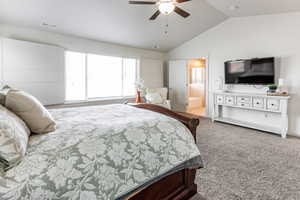 Primary bedroom with carpet, ceiling fan, connected bathroom, and vaulted ceiling