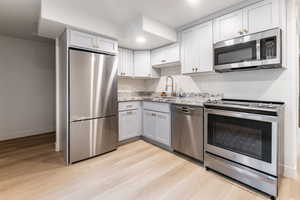 Kitchen featuring appliances with stainless steel finishes, light hardwood / wood-style flooring, light stone counters, and sink