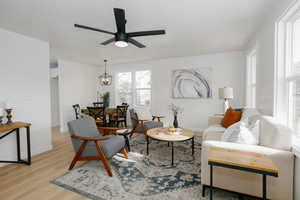 Living room with ceiling fan with notable chandelier and light hardwood / wood-style floors