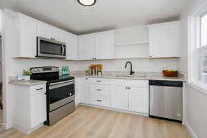 Kitchen with a wealth of natural light, white cabinetry, sink, light hardwood / wood-style floors, and appliances with stainless steel finishes