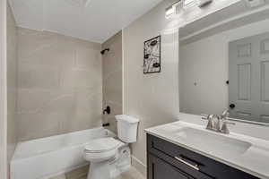 Full bathroom featuring a textured ceiling, vanity, toilet, and tiled shower / bath