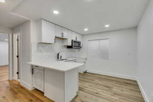 Kitchen with sink, kitchen peninsula, decorative backsplash, light wood-type flooring, and white cabinetry