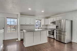 Kitchen with light stone countertops, appliances with stainless steel finishes, sink, white cabinets, and a center island