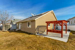 Rear view of property featuring a lawn, solar panels, a pergola, a storage shed, and a patio