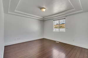 Unfurnished room with a tray ceiling, dark hardwood / wood-style flooring, and a textured ceiling