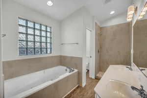 Full bathroom with vanity, vaulted ceiling, separate shower and tub, hardwood / wood-style floors, and toilet