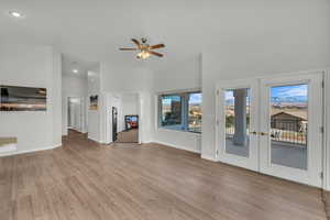 Unfurnished living room with french doors, light wood-type flooring, vaulted ceiling, and ceiling fan