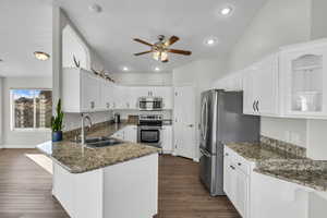 Kitchen featuring sink, stainless steel appliances, kitchen peninsula, dark stone countertops, and white cabinets