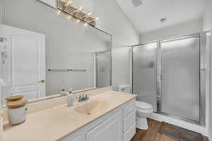 Bathroom with vaulted ceiling, toilet, vanity, a shower with shower door, and hardwood / wood-style flooring