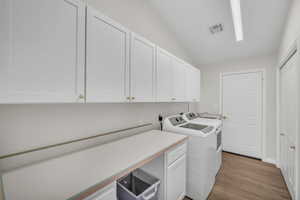 Clothes washing area with washer and dryer, cabinets, and light wood-type flooring