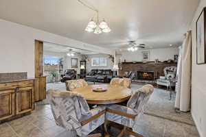 Dining space with a fireplace and ceiling fan with notable chandelier