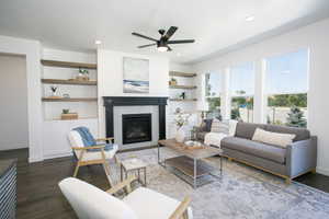 Living room featuring built in shelves, ceiling fan, a fireplace, and dark wood-type flooring