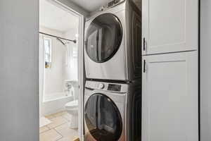 Washroom with stacked washer / drying machine and light tile patterned flooring