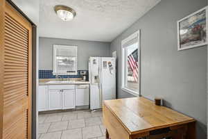 Kitchen with a textured ceiling, white cabinetry, white appliances, and sink