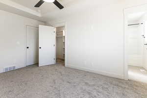 Unfurnished bedroom with a walk in closet, ceiling fan, ensuite bathroom, and light colored carpet