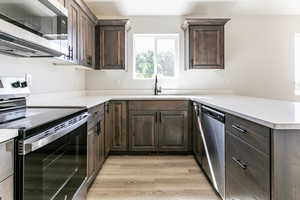 Kitchen featuring kitchen peninsula, dark brown cabinets, stainless steel appliances, sink, and light hardwood / wood-style flooring