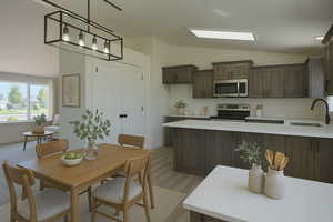Kitchen with dark brown cabinets, appliances with stainless steel finishes, a sink, light countertops, and vaulted ceiling