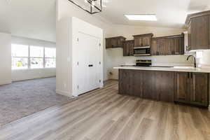 Kitchen featuring dark brown cabinetry, sink, kitchen peninsula, vaulted ceiling, and appliances with stainless steel finishes