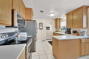 Kitchen with light tile patterned flooring, sink, stainless steel appliances, and light brown cabinets