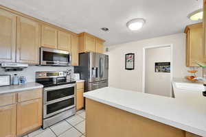 Kitchen featuring sink, light tile patterned floors, light brown cabinets, and appliances with stainless steel finishes