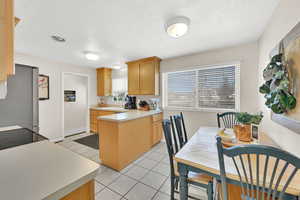 Kitchen featuring stainless steel fridge, stove, a textured ceiling, light brown cabinetry, and light tile patterned floors