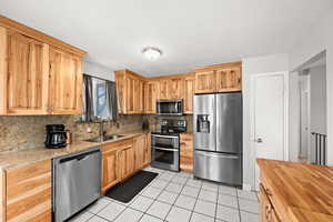 Kitchen with sink, stainless steel appliances, light stone counters, backsplash, and light tile patterned flooring