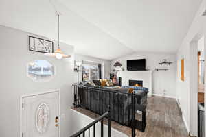 Living room with hardwood / wood-style flooring, lofted ceiling, and a brick fireplace