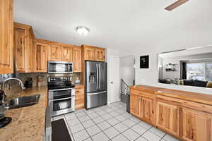 Kitchen with backsplash, sink, light stone countertops, light tile patterned floors, and stainless steel appliances