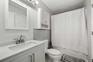 Full bathroom featuring vanity, shower / bath combo, backsplash, and toilet