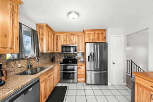 Kitchen with light stone countertops, sink, stainless steel appliances, tasteful backsplash, and light tile patterned flooring