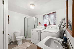 Bathroom with washing machine and dryer, tile patterned floors, a textured ceiling, toilet, and a shower with door