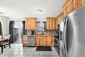 Kitchen featuring decorative backsplash, light stone counters, stainless steel appliances, sink, and light tile patterned floors