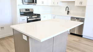Kitchen featuring light hardwood / wood-style floors, a kitchen island, white cabinetry, and appliances with stainless steel finishes