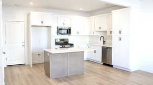 Kitchen with stainless steel appliances, a kitchen island, sink, light hardwood / wood-style floors, and white cabinetry