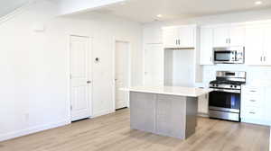 Kitchen with white cabinetry, light hardwood / wood-style flooring, a kitchen island, and appliances with stainless steel finishes