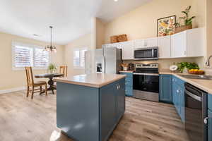 Kitchen featuring hanging light fixtures, appliances with stainless steel finishes, sink, white cabinets, and a kitchen island