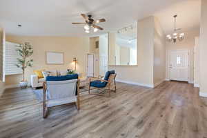 Living room with light hardwood / wood-style floors, ceiling fan with notable chandelier, track lighting, and vaulted ceiling