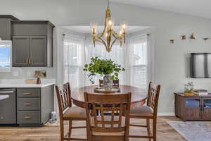 Dining space with light hardwood / wood-style floors, an inviting chandelier, and lofted ceiling