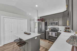 Kitchen featuring gray cabinetry, a breakfast bar, lofted ceiling, light hardwood / wood-style flooring, and appliances with stainless steel finishes